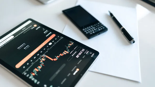 Close-up of a tablet displaying financial charts with a phone and pen on a white surface. Measuring marketing mix modeling: a staged scorecard with six gates