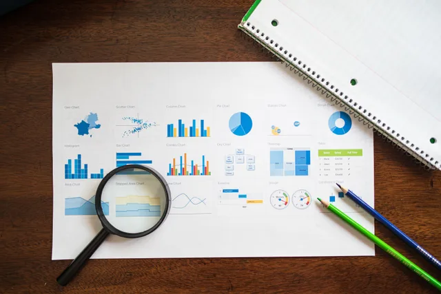 Overhead view of charts and graphs with magnifying glass and stationery on wooden table. How to log marketing attribution trends as testable changes