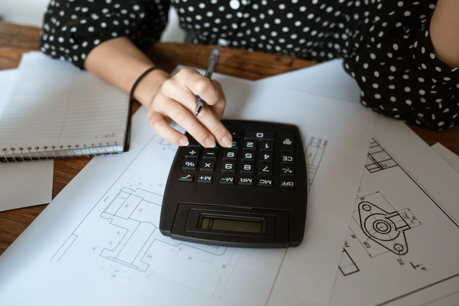 Close-up of an architect's hand using a calculator on technical drawings with a polka dot shirt. Marketing KPIs for people who want the details